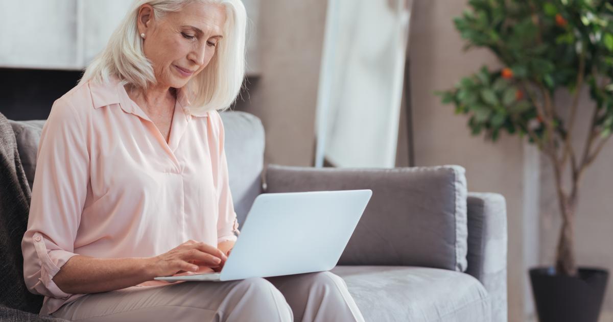 Older woman with pink blouse sitting on couch looking at laptop